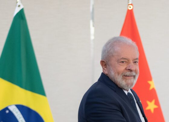 Imagem colorida de Lula com as bandeiras brasileira e chinesa ao fundo